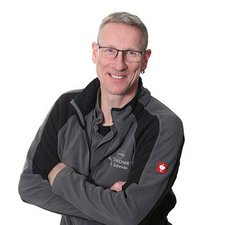 Freundliches Porträt eines Mannes mit Brille Ein freundlicher Mann mit Brille und kurzen Haaren steht lächelnd vor einer neutralen weißen Wand, die seine Persönlichkeit unterstreicht.