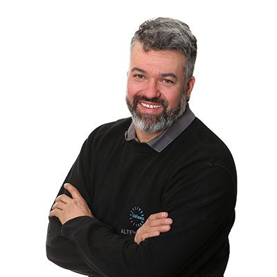 Ein lächelnder Mann mit grauem Bart und kurzen Haaren, der in einem schwarzen Pullover mit Logo posiert.